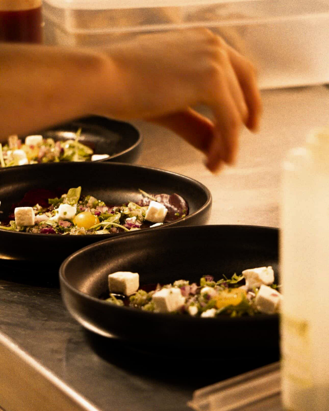Main déposant une touche de finition sur deux assiettes de gastronomie dans des bols noirs, photographie culinaire par Aptitude Pro.