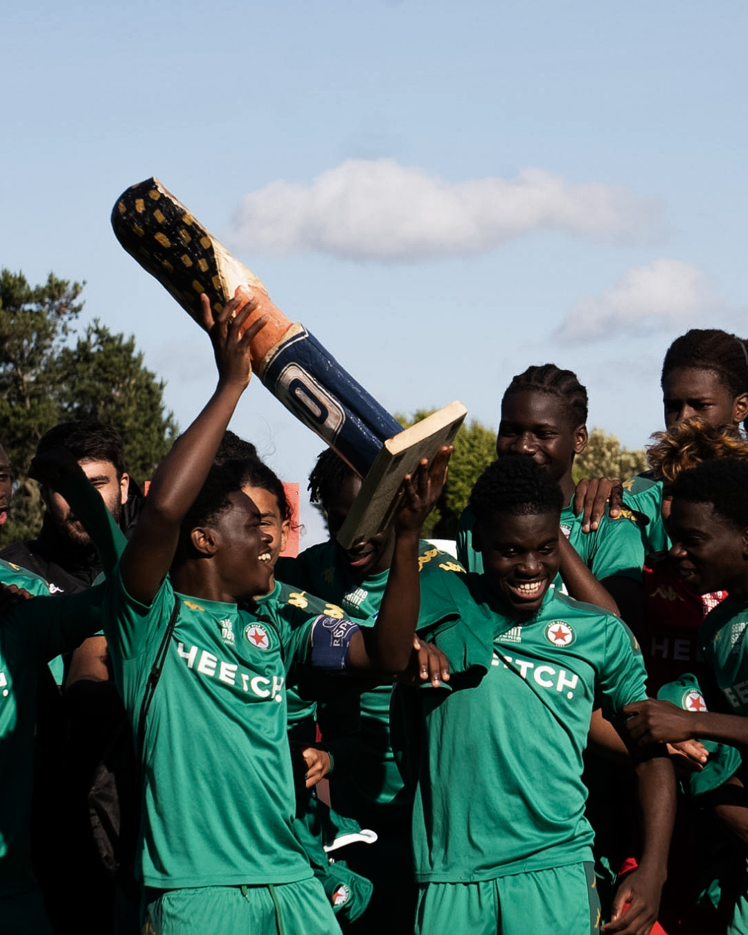 Joueurs en maillot vert soulevant un trophée en signe de victoire, photographie de célébration sportive par Aptitude Pro.