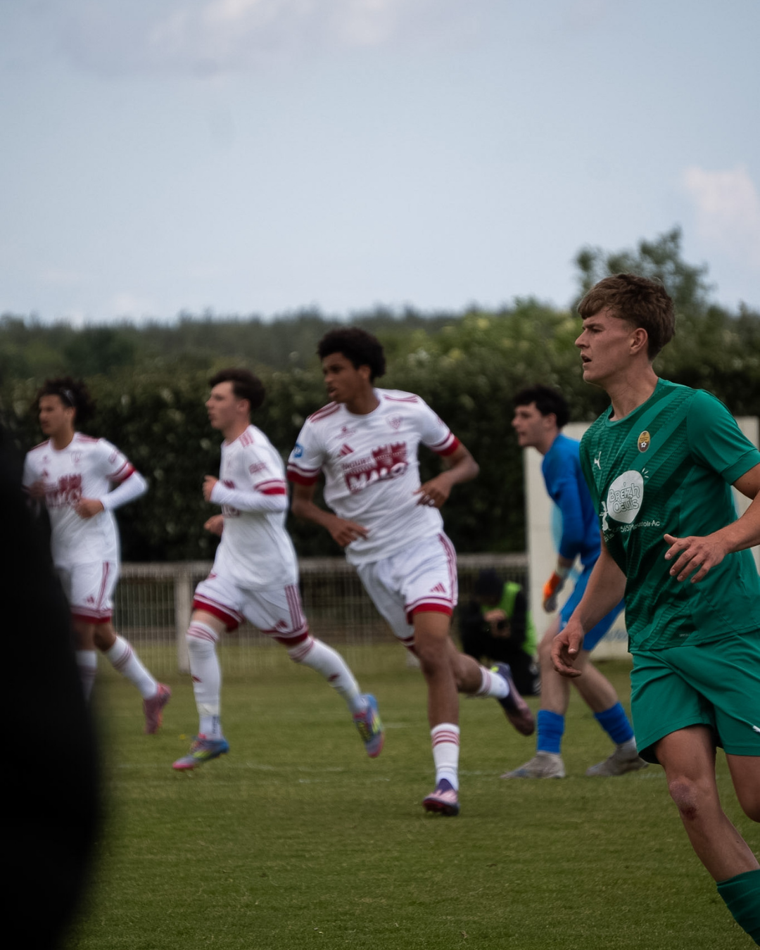 Action de match de football entre joueurs en maillots blanc et vert, reportage sportif par Aptitude Pro.