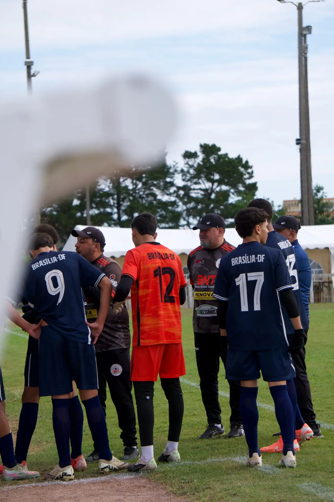 Deux équipes de football en maillots bleu marine et rouge se faisant face, vue à travers l'objectif d'une caméra, reportage sportif par Aptitude Pro.