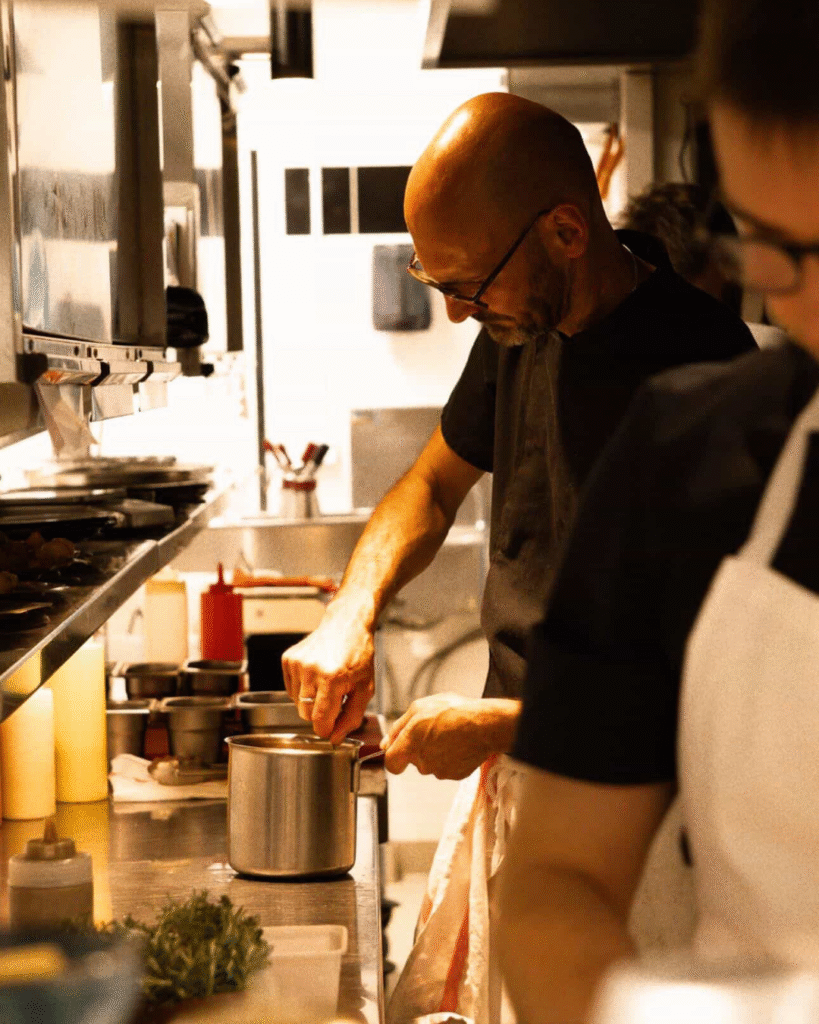Chef cuisinier préparant un plat en cuisine, photographie culinaire en noir et blanc réalisée par Aptitude Pro.